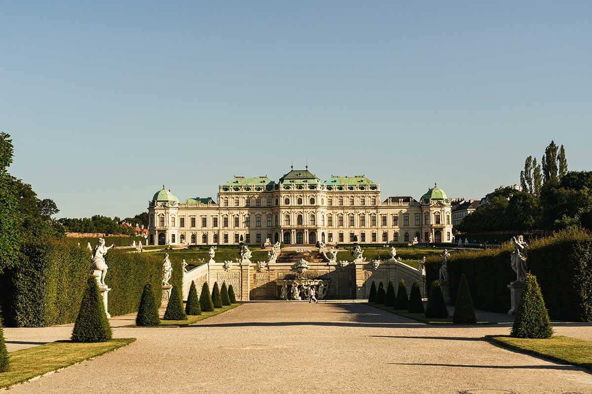 Das Barockschloss Belvedere in Wien mit grüner Hecke und Statuen im Garten.