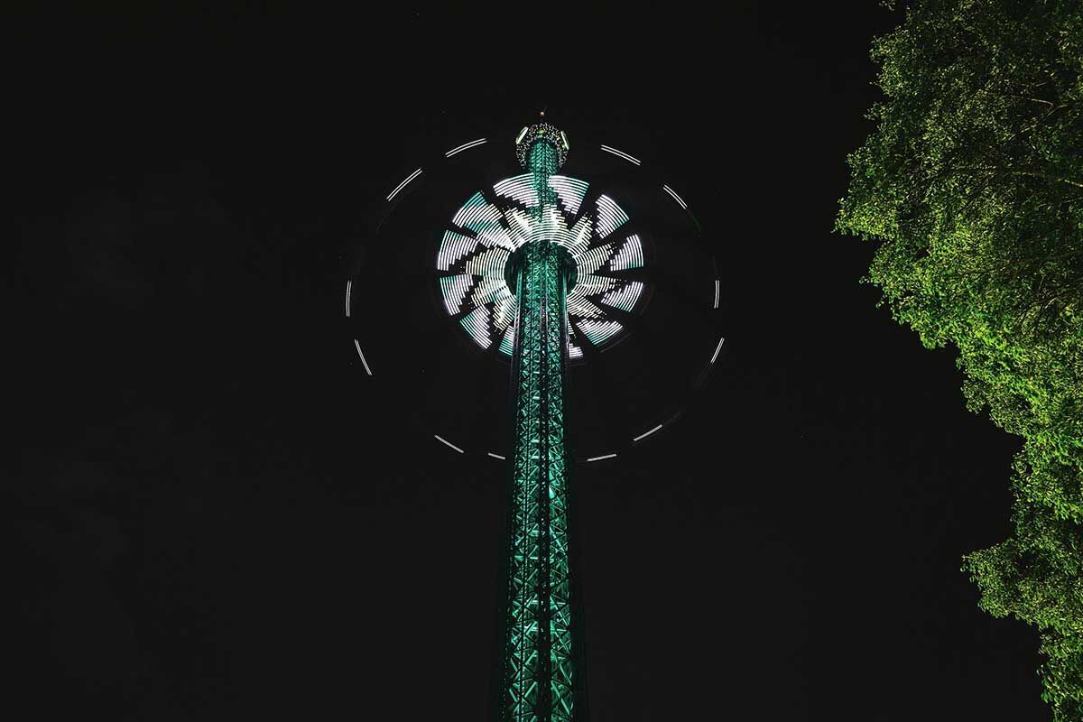 Beleuchteter Fahrgastturm über das nächtliche Stadtbild mit Bäumen.