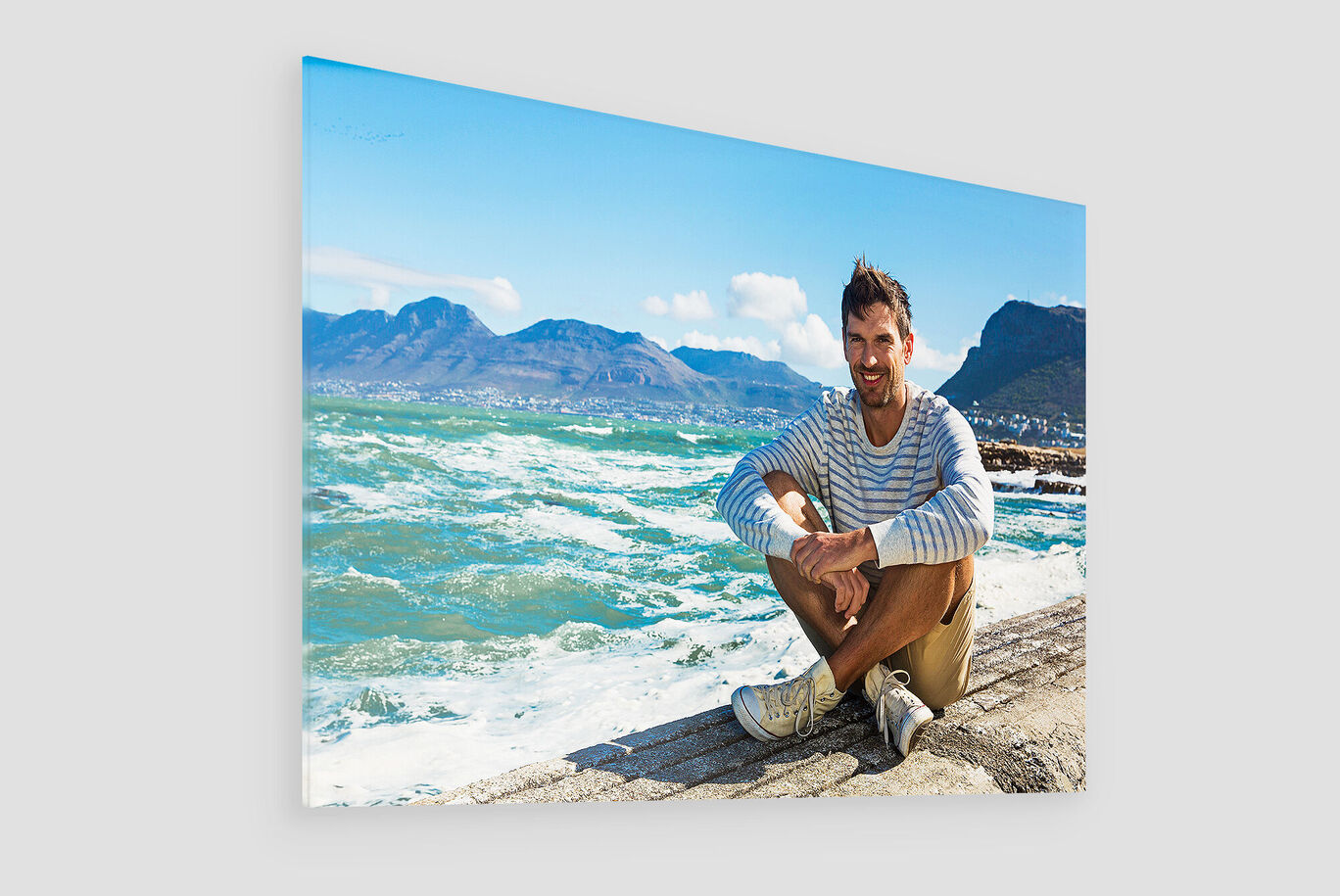 Eine Person sitzt am Strand und genießt den Ausblick auf die Wellen und Berge. Es ist sonnig und die Stimmung ist entspannt.