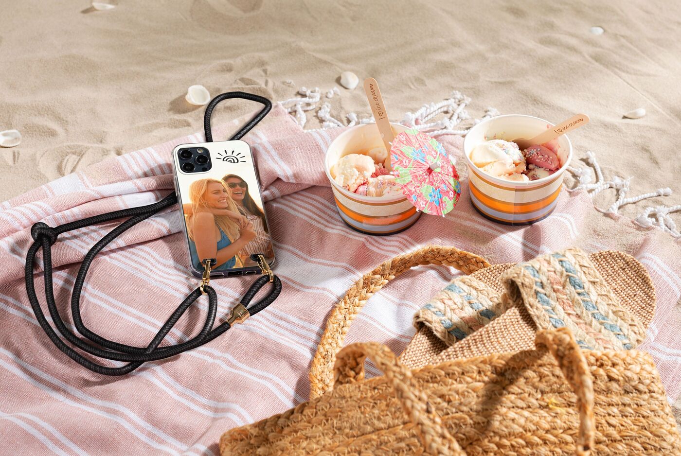 Eine Smartphone-Hülle liegt am Strand neben zwei Schalen mit Eiscreme auf einem handgewebten Tuch.