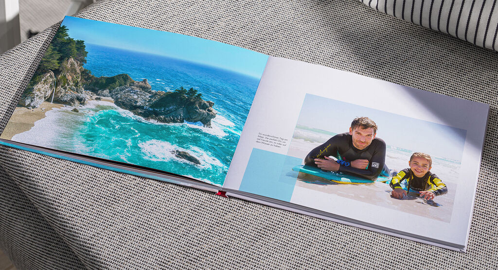 Offenes Fotobuch mit Strandurlaubserinnerungen auf einer Couch