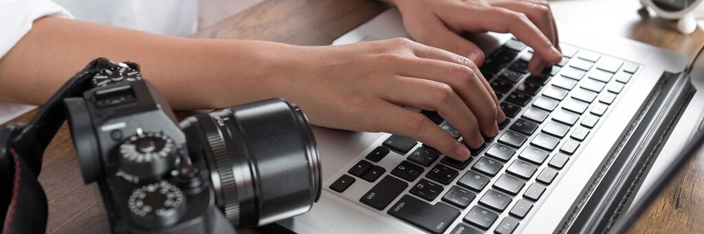 Person, die an einem Laptop tippt, neben einer Kamera