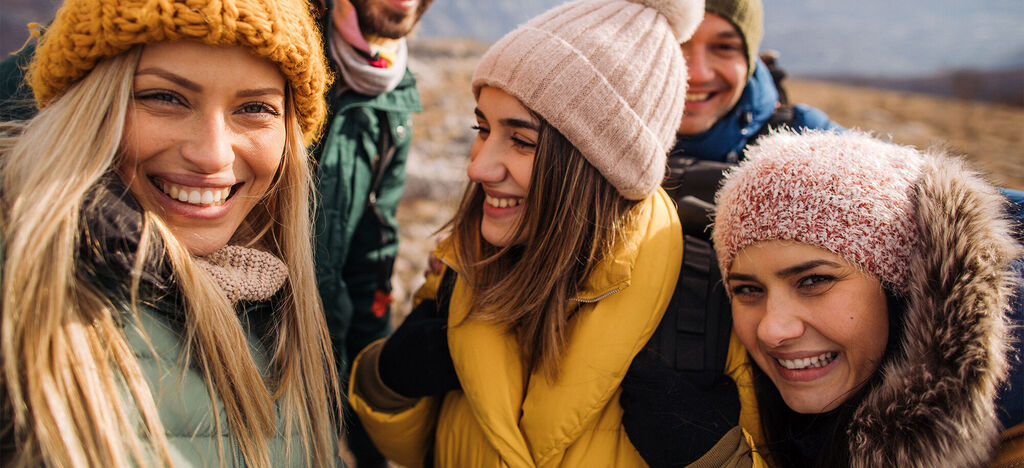 Gruppe von Freunden bei einem Ausflug in der Natur, jeder trägt winterliche Kleidung, fröhliche Stimmung, harmonische Umarmung.
