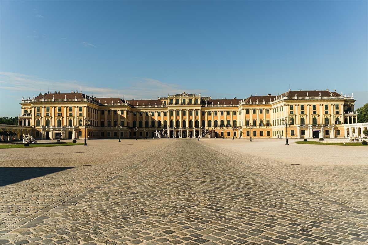 Das Schloss Schönbrunn in Wien strahlt majestätisch in der Sonne. Der große Vorplatz ist umgeben von bunten Blumen.