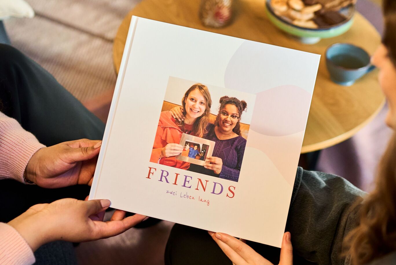 Zwei Personen zeigen stolz ein Fotobuch mit dem Titel "FRIENDS"