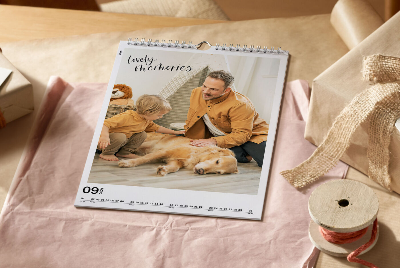 Ein Familienkalender auf einem Tisch. Darauf liegen ein Kind und ein Hund, während ein Erwachsener ihnen Gesellschaft leistet. Der Monat ist September.