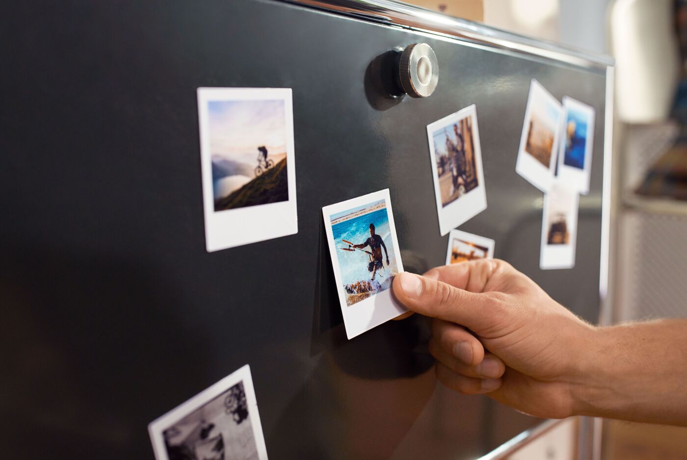 Eine Hand hängt ein Foto an einen Kühlschrank mit mehreren Bildern.