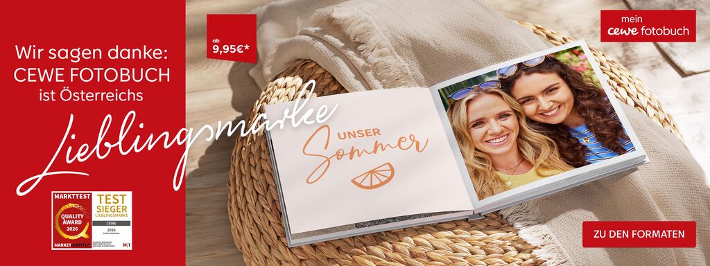 Ein aufgeschlagenes CEWE FOTOBUCH liegt auf einem Sessel mit Decke. Es sind zwei Frauen zu sehen und der Schriftzug "Unser Sommer"