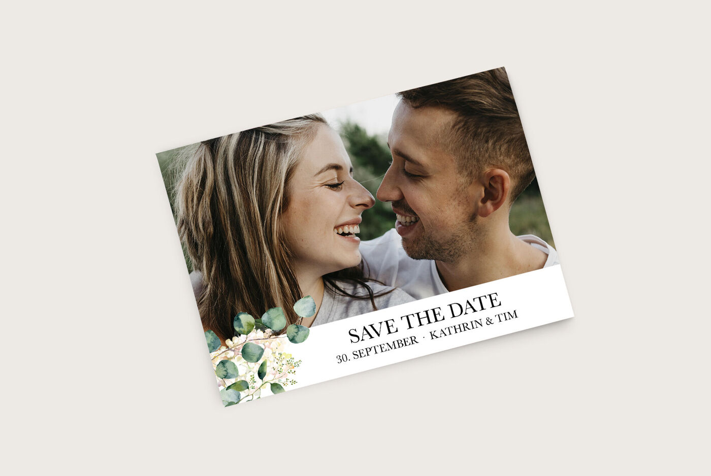 Ein Paar hält sich in der Natur umarmt, um den "Save the Date"-Anlass zu feiern. Elegantes Design mit grünen Elementen und einem wunderschönen Schriftzug.
