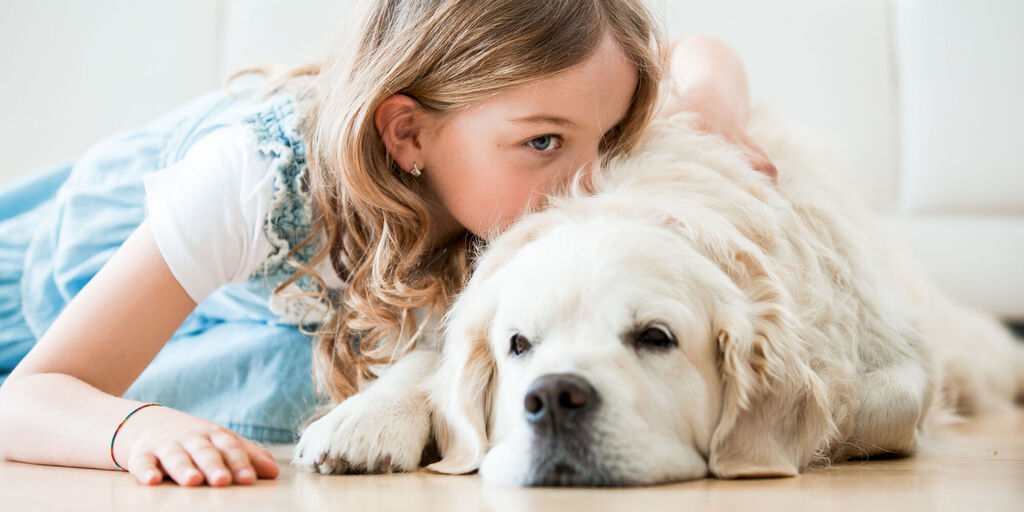 Ein Kind mit langen, lockigen Haaren liegt neben einem großen, freundlichen Hund. Der Hund schaut entspannt und glücklich.