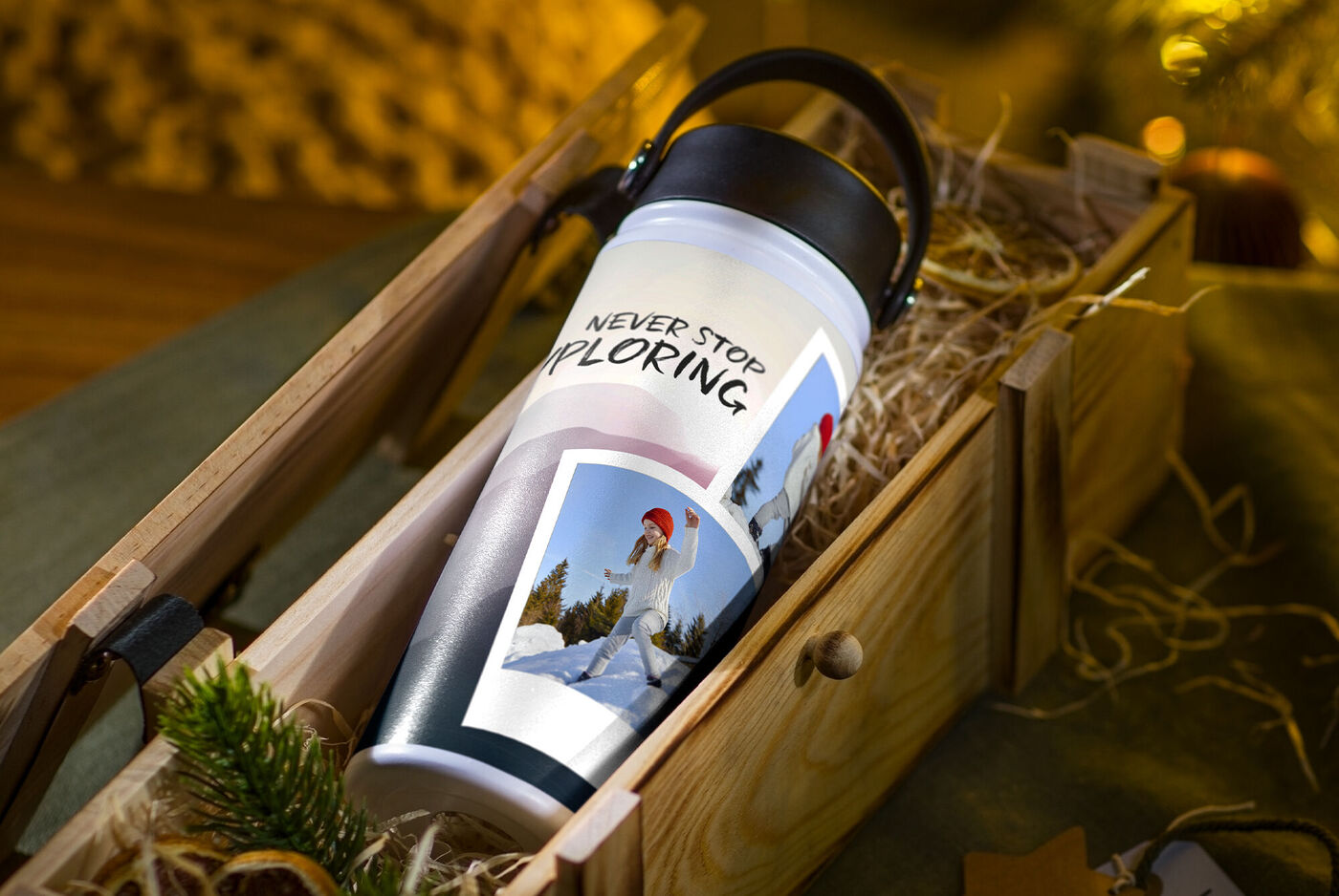 Ein bunter Becher liegt auf Holzwolle in einer Holzkiste, umgeben von festlicher Dekoration. Der Becher zeigt eine inspirierende Botschaft zum Entdecken.
