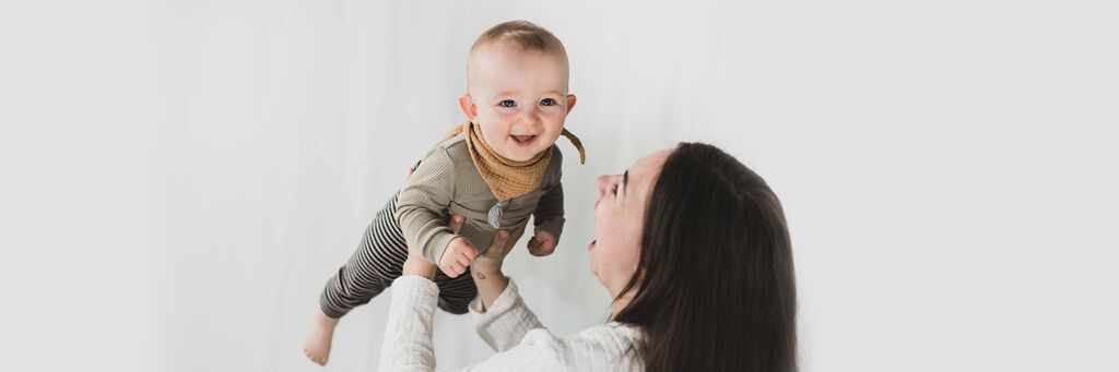Eine Mutter hebt ihr Kind freudig in die Luft.