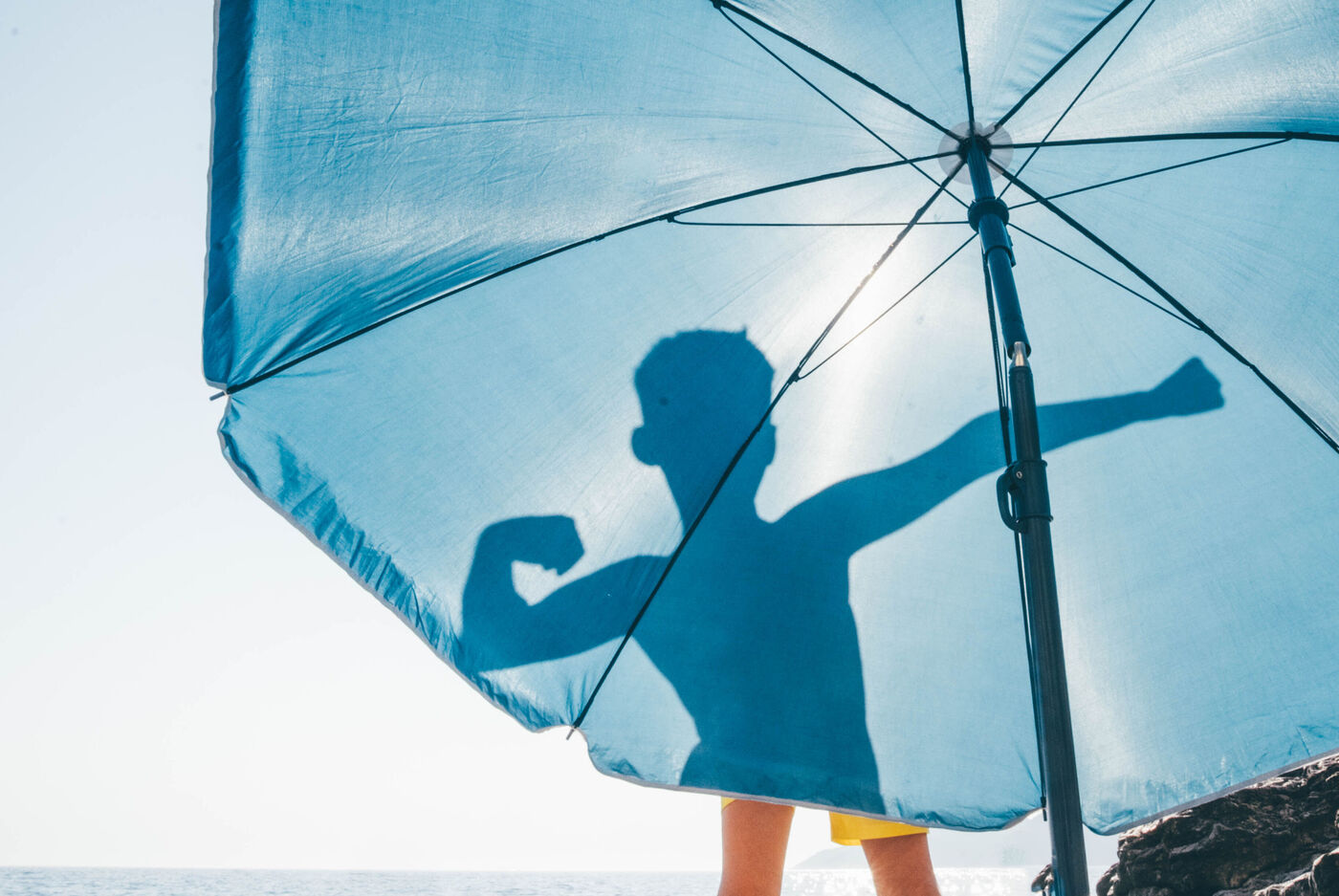 Blauer Sonnenschirm am Strand, mit der Silhouette einer Person im Hintergrund