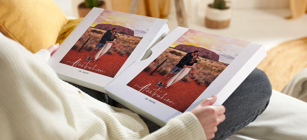 Eine Person hält zwei CEWE Fotobücher in der Hand, umgeben von Natur.