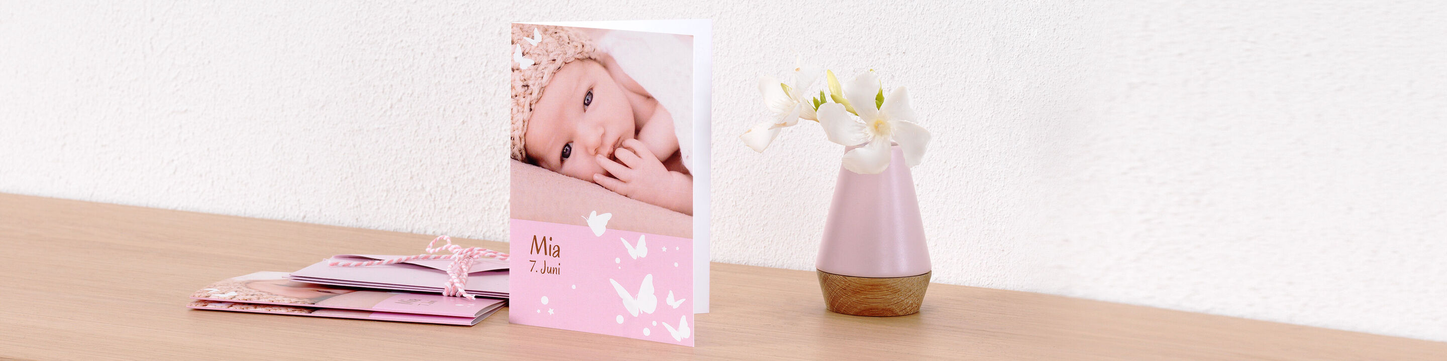 Eine liebevoll gestaltete CEWE Grußkarte mit einem Babyfoto. Die Karte hat einen rosa Hintergrund mit zarten Schmetterlingen.