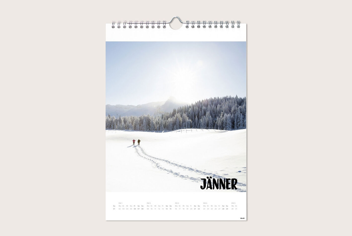 Zwei Menschen gehen auf einem verschneiten Feld im Januar, umgeben von schneebedeckten Bäumen und Bergen