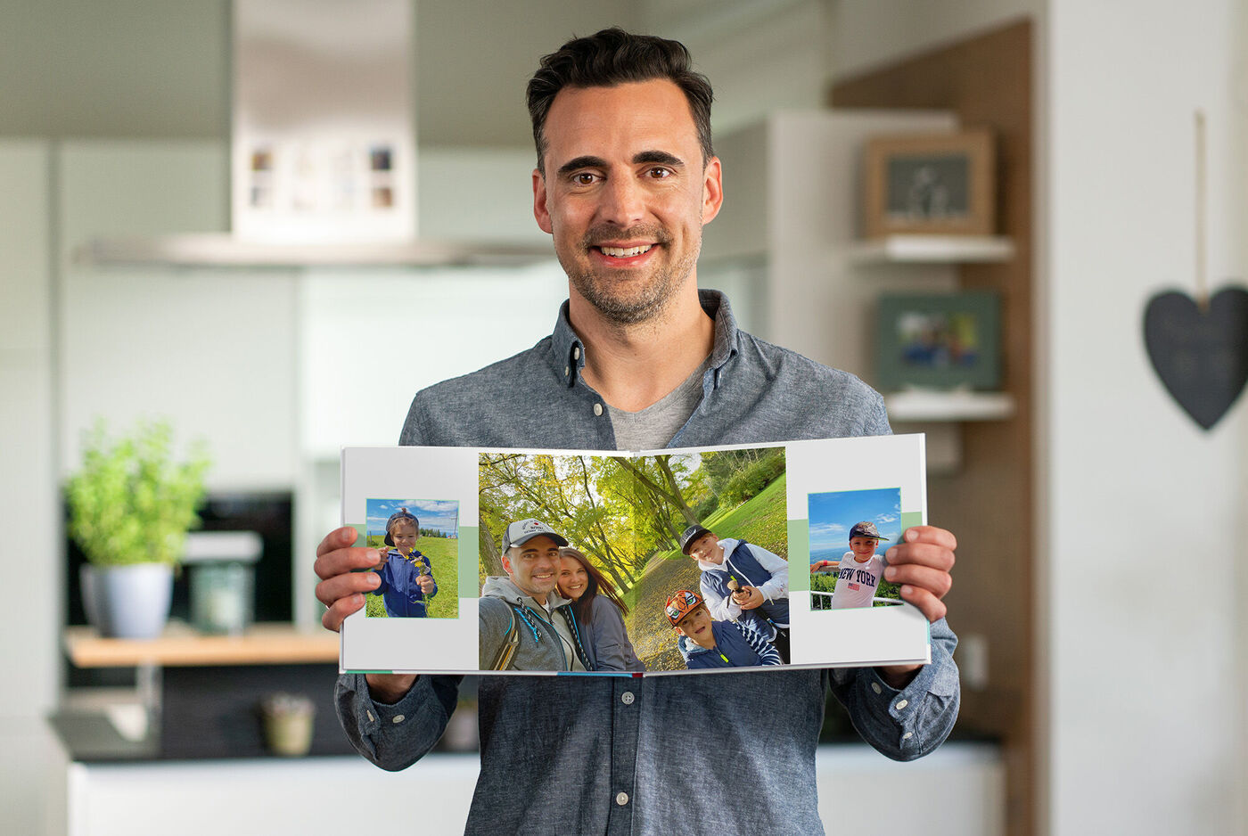 Person hält ein aufgeschlagenes CEWE FOTOBUCH mit Fotografien von glücklichen Momenten im Freien