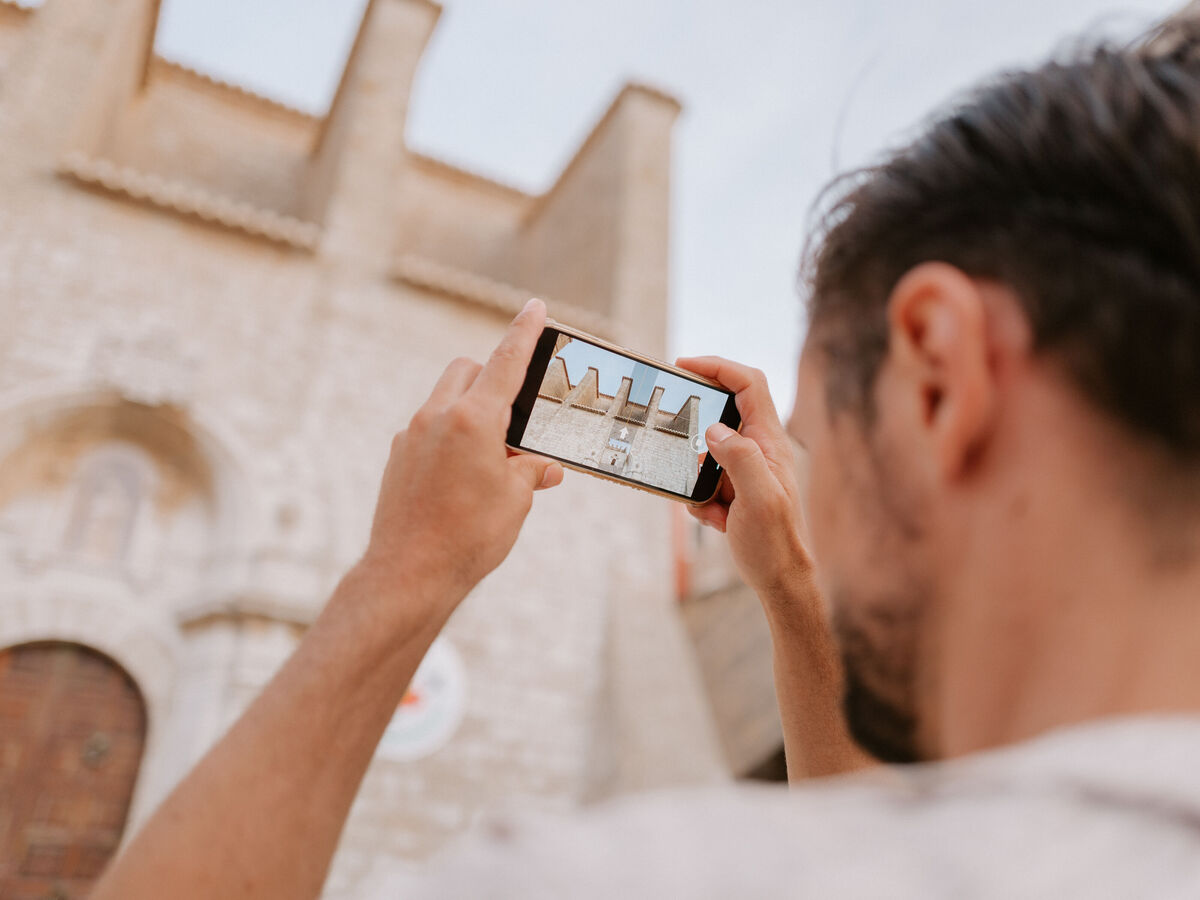 Person hält ein Smartphone und fotografiert die Fassade eines historischen Gebäudes aus hellem Stein.