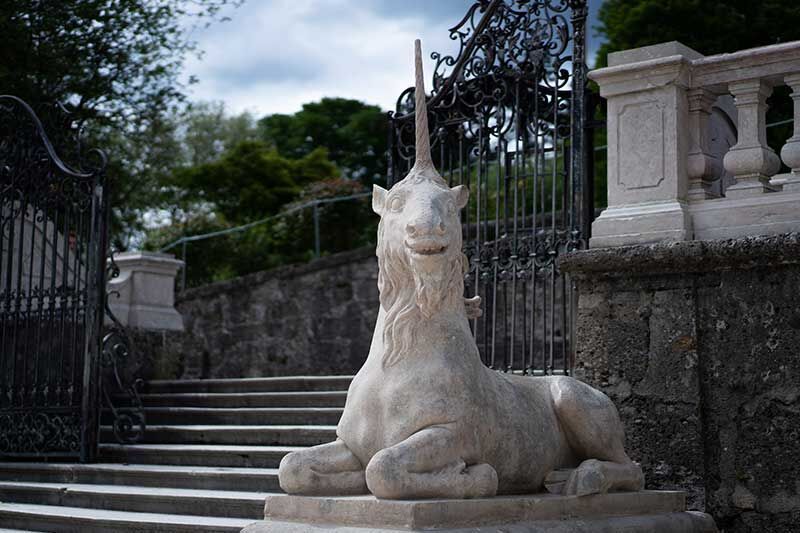 Ein majestätisches Steineinhorn sitzt an einer Treppe vor einem prachtvollen Tor.