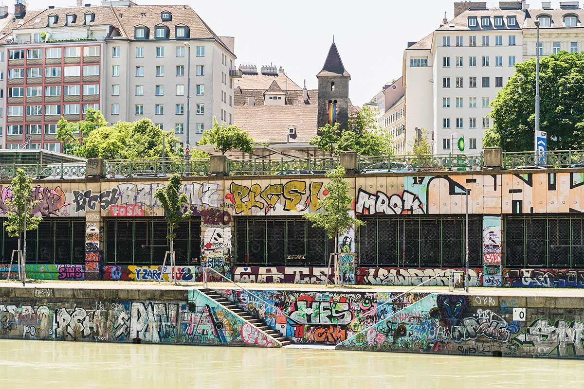 Bunte Graffiti an einer Gebäudefassade entlang eines ruhigen Flusses