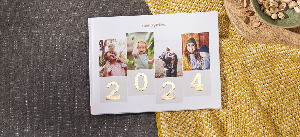 Ein CEWE FOTOBUCH mit goldenen Zahlen für das Jahr 2024 und drei Fotos von glücklichen Menschen.