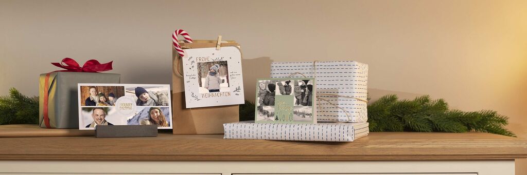 Eine schön dekorierte Holzoberfläche mit Geschenken in buntem Papier und einem personalisierten Foto-Poster von CEWE zwischen den Päckchen.