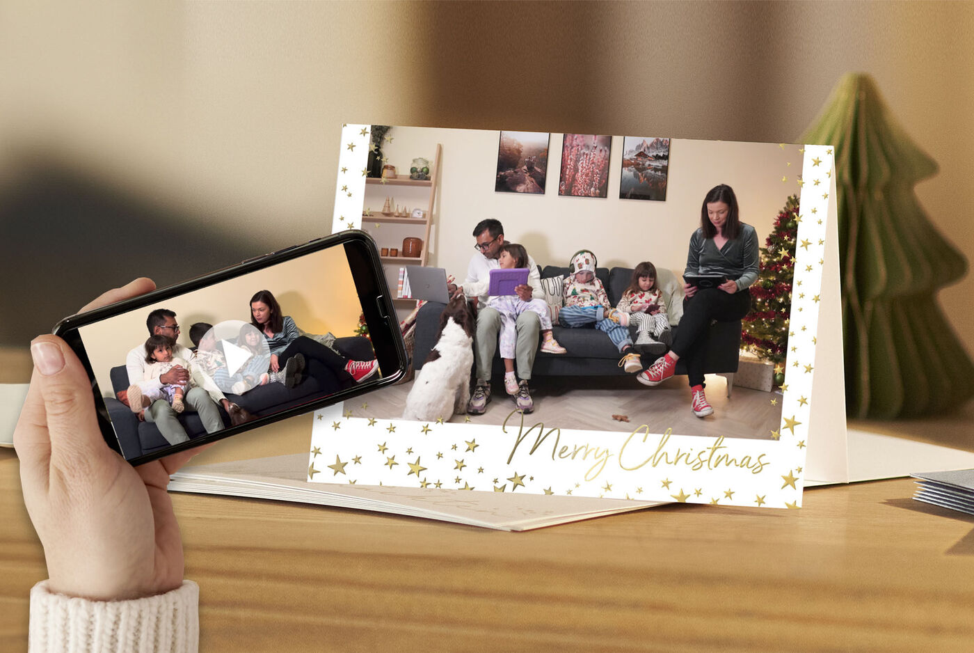 Eine Weihnachtskarte mit Familienfoto auf einem Tisch. Davor eine Hand mit Smartphone auf dem eine Videobotschaft abgespielt wird.