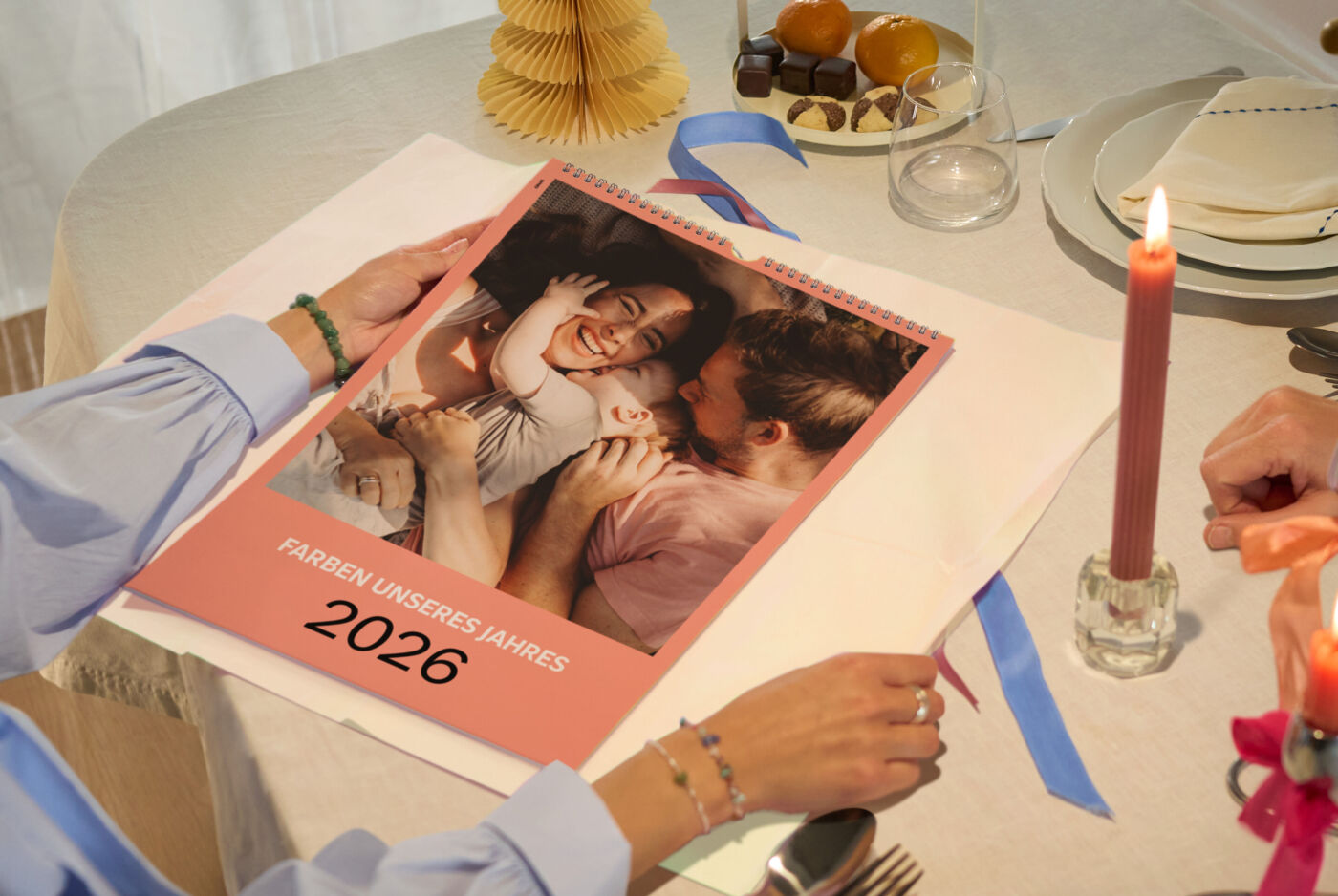 Zwei Personen am festlich gedeckten Tisch betrachten einen CEWE Fotokalender mit Familienfotos