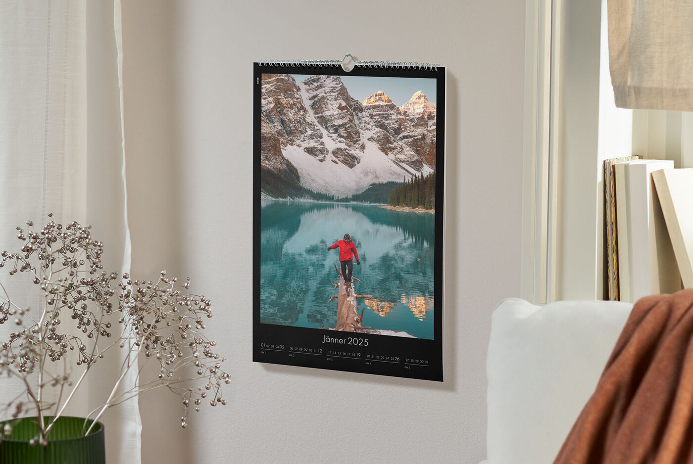 Ein Wandkalender zeigt einen Bergsee mit schneebedeckten Bergen und einem Wanderer in roter Jacke im Vordergrund.