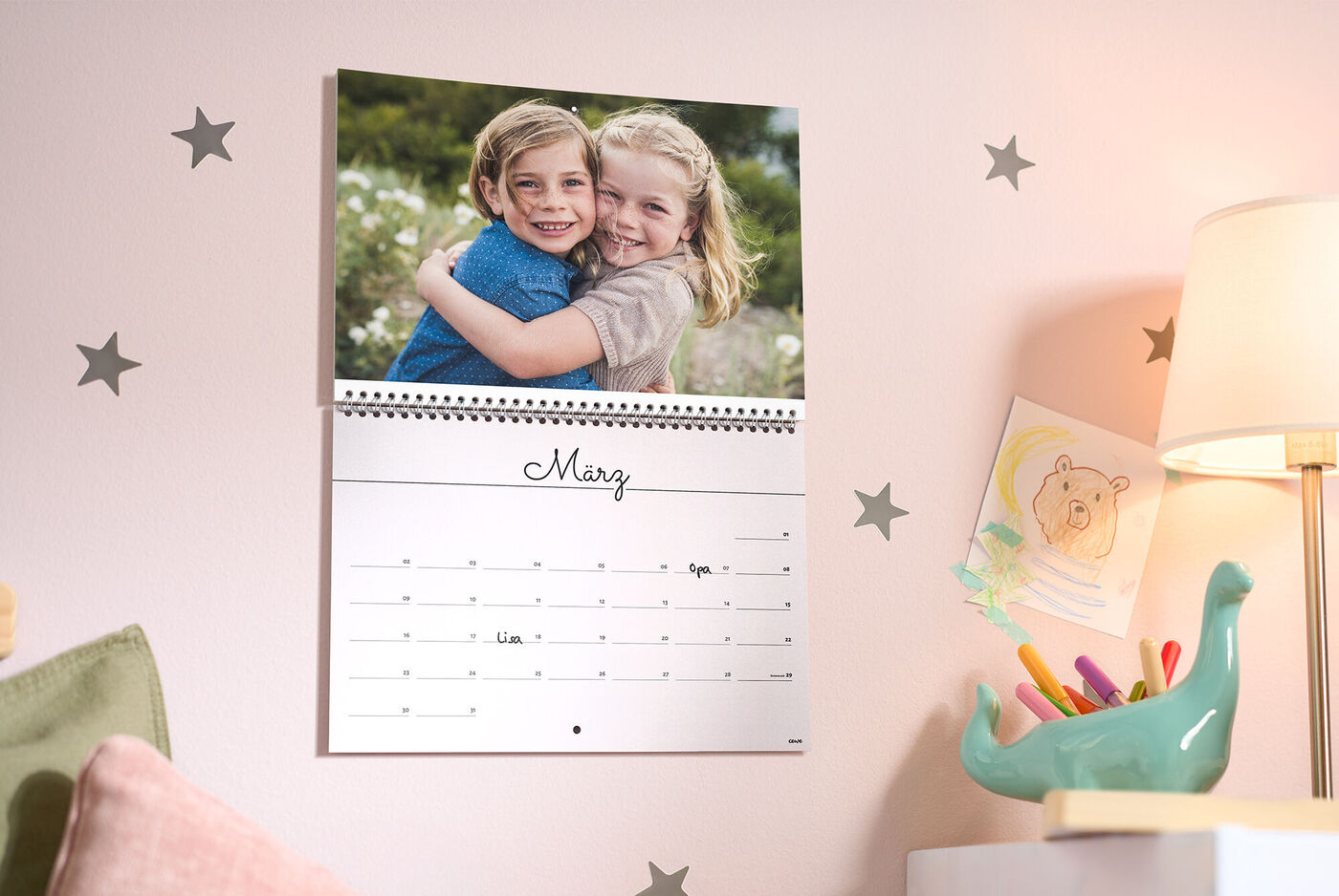 Ein CEWE Fotokalender hängt an der Wand und zeigt ein liebevolles Foto zweier Kinder sowie den Monat März.