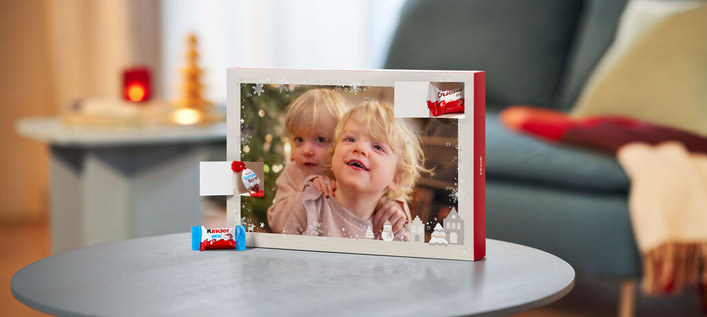 Ein CEWE Adventskalender gefüllt mit Schokolade von kinder, offenen Türchen und einem Foto von 2 Kindern.
